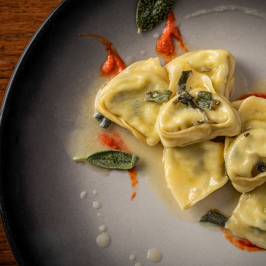 Ravioli garnished with fresh sage on a dark plate