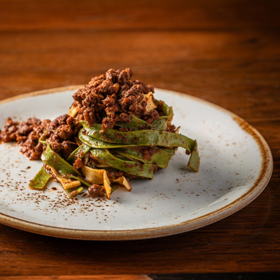 Green tagliatelle topped with meat ragù on a ceramic plate